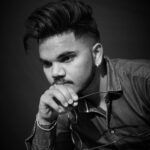 Black and white portrait of a thoughtful man with stylish hair, holding eyeglasses.